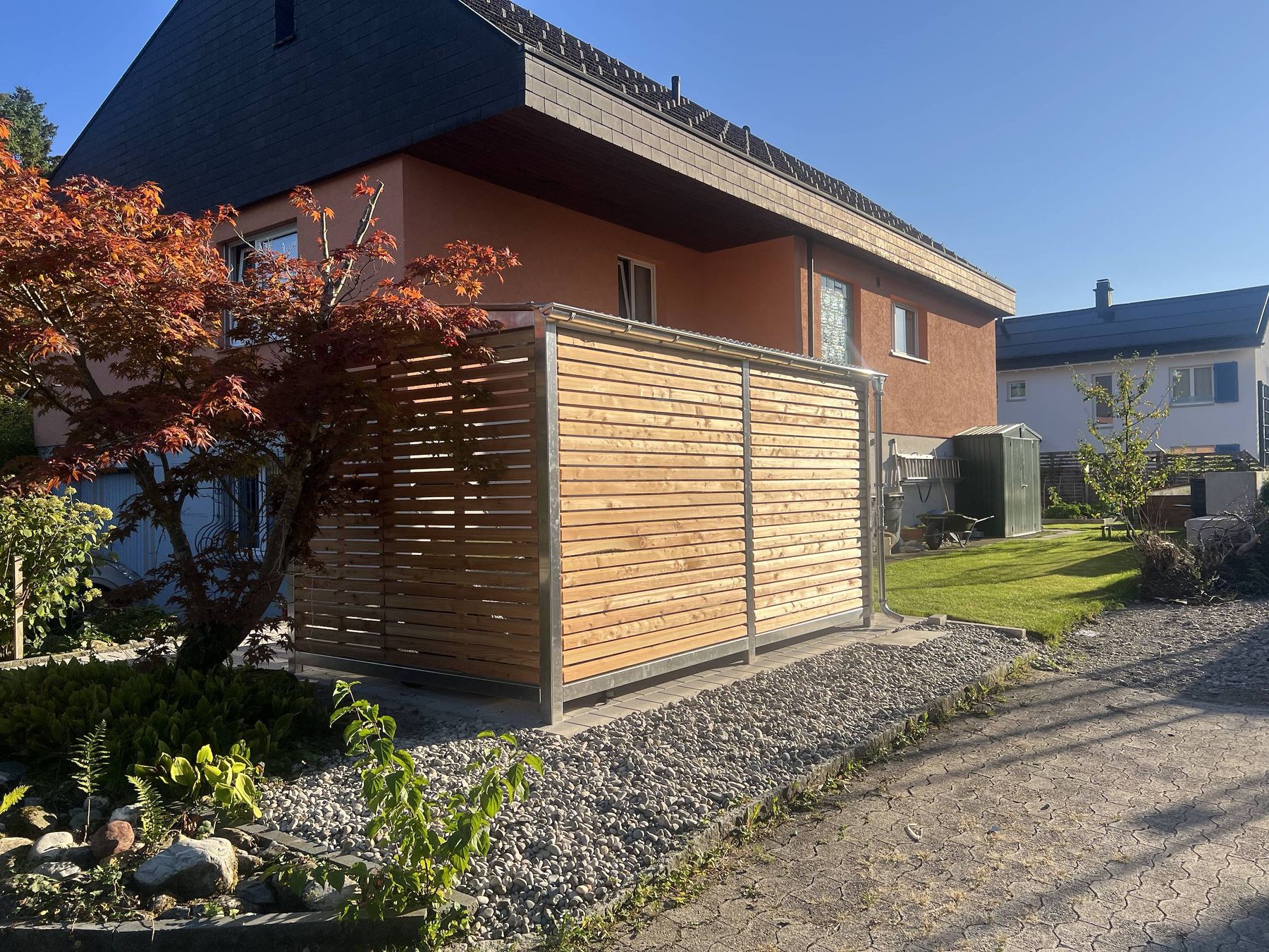 Velounterstand neben einem Wohnhaus, davor ein roter Ahorn